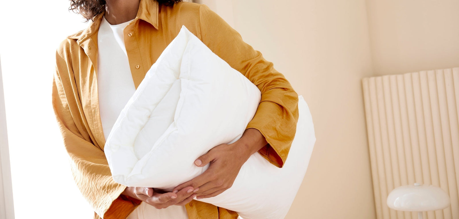 Personne tenant un oreiller Wopilo plus dans ses bras, dans une pièce lumineuse aux tons clairs, illustrant le confort et le choix d’un nouvel oreiller.